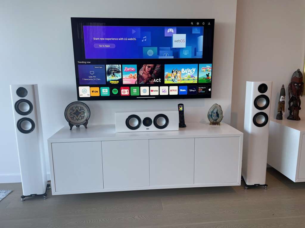 LG TV wall mounted above a wall mounted cabinet with ELAC speakers